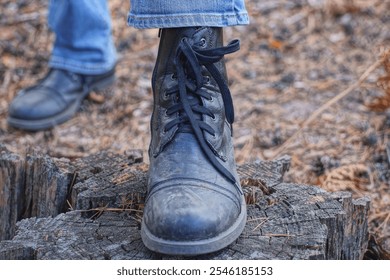 one black high army leather boot on a foot stands on a  gray stump in nature - Powered by Shutterstock