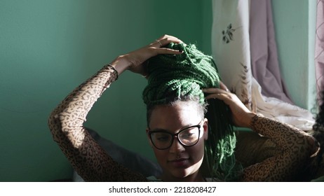 One Black Latina Adult Girl Playing With Braided Hairstyle. A Brazilian African American Young Woman Plays With Green Box Braid Hair At Home. Relaxed Emotion