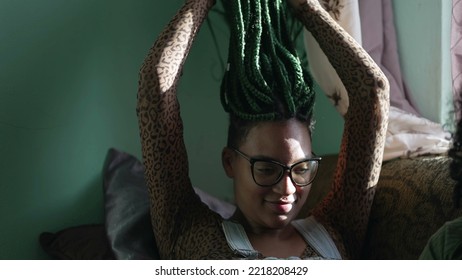 One Black Latina Adult Girl Playing With Braided Hairstyle. A Brazilian African American Young Woman Plays With Green Box Braid Hair At Home. Relaxed Emotion