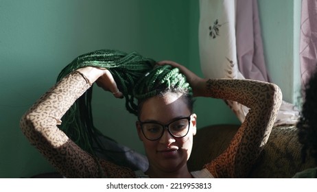 One Black Latina Adult Girl Playing With Braided Hairstyle. A Brazilian African American Young Woman Plays With Green Box Braid Hair At Home. Relaxed Emotion