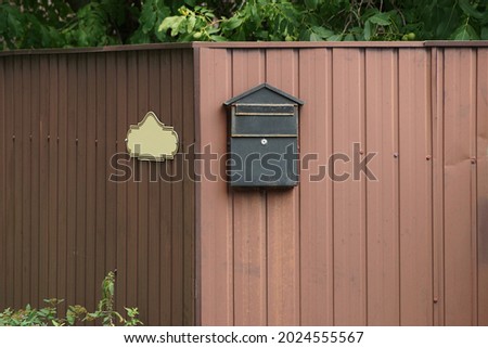 one black mailbox hanging on a brown metal fence wall in the street