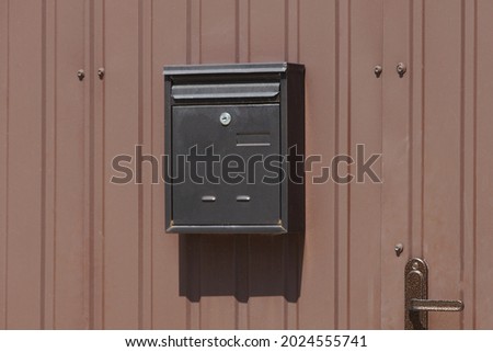 one black mailbox hanging on a brown metal fence 
