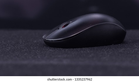 One black wireless optical mouse from the side in dim light on a dark background and table