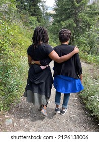 One Black Woman With Locs With Her Arm Around An Older Black Woman Walking On A Footpath In A Nature