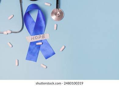 One blue ribbon with sticky tape with the word: hope, stethoscope and scattered pills on the left on a blue background with copy space on the right, flat lay close-up. Concept for world cancer day - Powered by Shutterstock