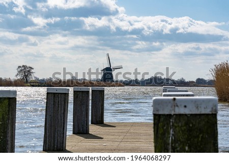 One of the boat docks with mooring posts in the lake de Rottemeren with the windmill Tweemanspolder nr 4 in the background on a sunny day with beautiful skies  