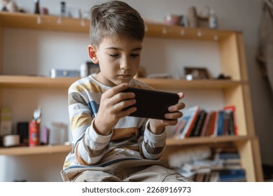 one boy caucasian child preschooler hold smartphone mobile phone at home play video games childhood and growing up technology addiction concept use smartphone app for online browsing or watch video - Powered by Shutterstock