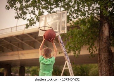 One Boy, Playing Basketball Alone, Holding A Ball In His Hands, Shooting To A Backboard. Upper Body, Rear View, Shot From Behind.