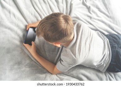 One Boy Teenager In A Gray Shirt Lies On The Couch On A Gray Plaid View From Above And Looks At A Mobile Phone