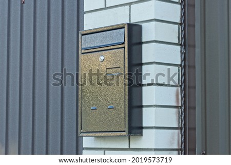 one brown iron mailbox on a white brick wall and a metal fence