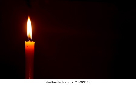 One candle burning bright against black background