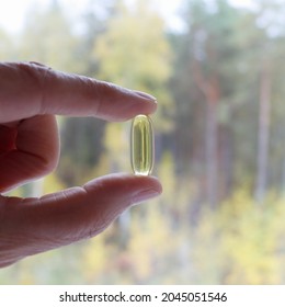 One Capsule Vitamin E  In Hand, Fish Oil, Omega-3 On A White Background Against The Backdrop Of The Landscape. Trees Are Reflected In The Capsule. Medicine, Healthcare And Pills Concept. Flatlay. 