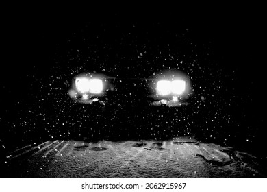 one car standing in the snow fall. night scene. back lit. The car goes on a snowy road on a dark black night in winter. Headlights brightly illuminate the path and the forest after a snowfall