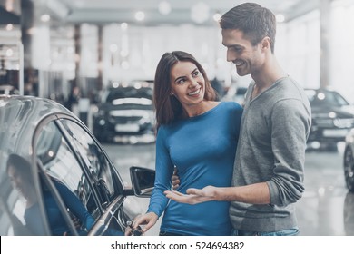 It is the one car I want! Beautiful young couple standing at the dealership choosing the car to buy