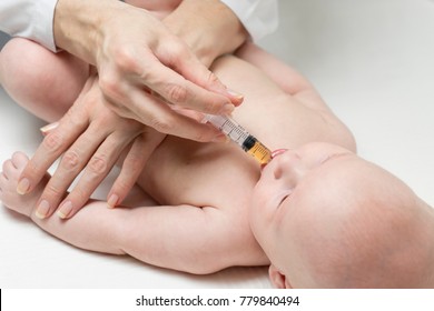 One caucasian female doctor is giving some dose of liquid medicine to infant baby boy by syringe into the mouth from disease or for vaccination at appointment.