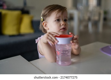 One Child Small Caucasian Toddler Female Baby Holding Plastic Cup Drink Water Alone At The Table At Home In Room Real People Copy Space Early Child Development Concept Learning Side View