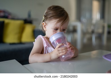 One Child Small Caucasian Toddler Female Baby Holding Plastic Cup Drink Water Alone At The Table At Home In Room Real People Copy Space Early Child Development Concept Learning Side View