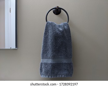 One Clean Blue Hand Towel Is Hanging On The Black Circle Hanger Beside The Mirror In The Bathroom. It Has Gray Background. Left Side Of The Picture Is Bright And Other Side Is Dark Because Of Shade