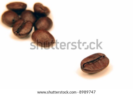 One coffee bean seperated from the a group of them on white.