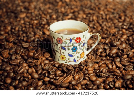One coffee cup inside the mass of scattered grains of black coffee. Still life in oriental style 