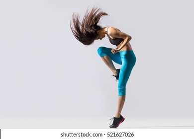 One cool beautiful young fit modern dancer lady in blue sportswear warming up, working out, dancing with her long hair flying, full length, studio image on gray background