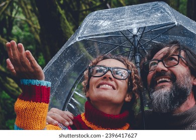 One couple have fun and enjoy bad weather rain under a transparent umbrella smiling together and checking drops water. Outdoor leisure activity in winter season for man and woman in friendship - Shutterstock ID 2396417627