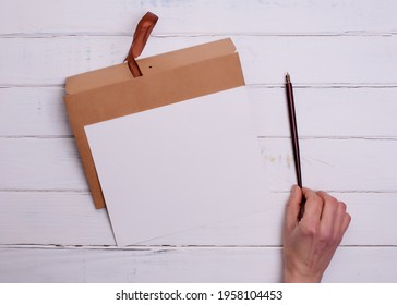 One Craft envelop, white paper t and ink pencil in hand on white   wooden background