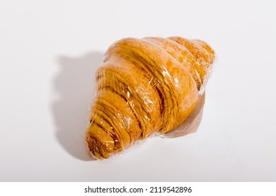 One Croissant On White Background With Black Shadow In Cling Film. High Quality Photo