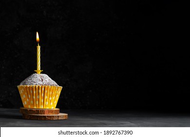 One cupcake in a paper cup with a yellow candle with flame on a dark background copy space birthday card