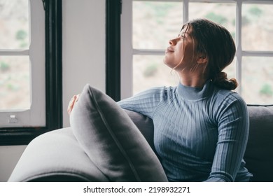 One cute and beautiful young girl looking outdoors at the window from the sofa relaxing and resting. Thoughtful woman pensive and thinking sitting on the couch. - Powered by Shutterstock