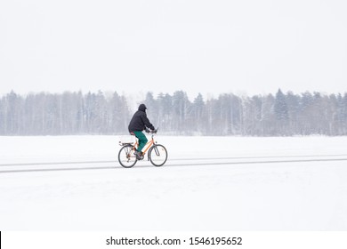 One Cyclist Biking Slowly And Hard In Blizzard. Old Man With Bike On Roadside Along Forest In White Winter Day. Poor Visibility In Heavy Snow Storm On Road. Side View.
