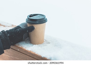 One disposable coffee cup on the snow on a wooden board. A hand in a knitted black glove holds a package - Powered by Shutterstock