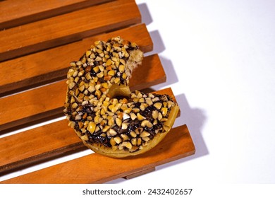 one donut with chocolate peanut topping, on a wooden coaster and a plain white backgorund - Powered by Shutterstock