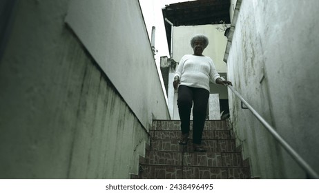 One elderly black lady from South American stepping out into sidewalk from residence. 80s female person of African descent going down the stairs and opens front door going out for daily routine - Powered by Shutterstock