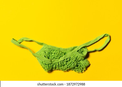 One Empty Green Mesh Bag On Bright Yellow Paper Background. Flat Lay. Horizontal Orientation. Conscious Consumerism And Eco Friendly Shopping Concept. Copy Space.