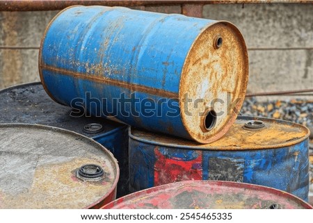 one empty rusty open  blue discarded round industrial painted iron old oil hazardous barrel lies on other barrels in a dump during the day on the street