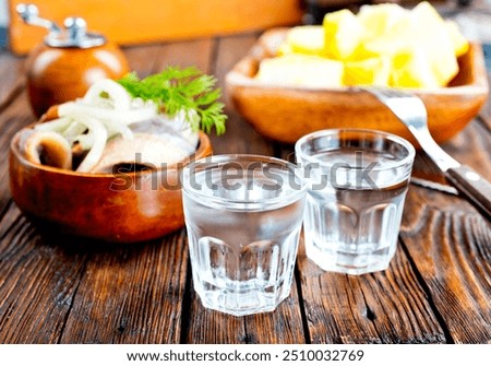 one empty second vodka-filled glass surrounded by a snack with herring and onions, a plate with fish and herbs on a wooden background