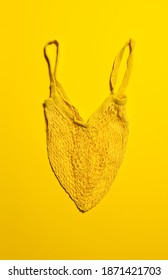 One Empty Yellow Mesh Bag On Bright Yellow Paper Background. Flat Lay. Vertical Orientation. Conscious Consumerism And Eco Friendly Shopping Concept.