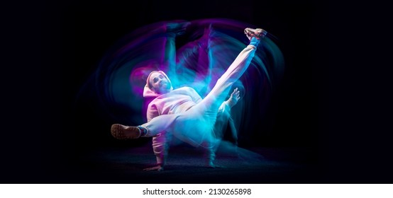 One energy young flexible sportive man dancing hip-hop or breakdance in white outfit on dark background in mixed blue neon light. Concept of sport, art, action, moves, youth culture. Banner for ad