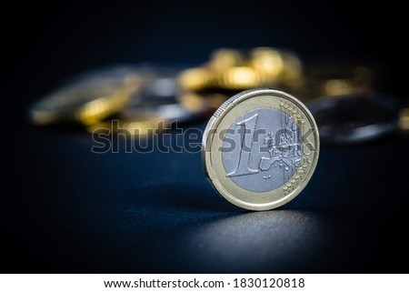One Euro coin on black background, with many coins blurred in the background. Selective focus - shallow depth of field.