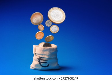 One Euro coins falling into bag over blue background with copy space
