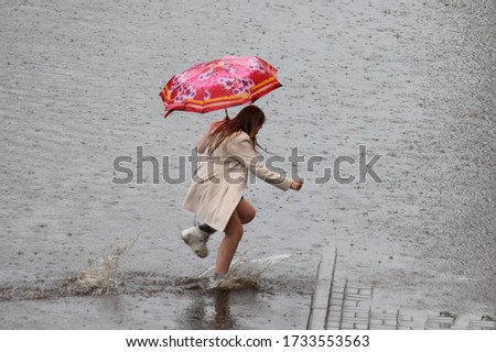 A one European girl under an umbrella in a short coat runs in white sneakers through a large puddle in heavy rain on spring day on city street Stock photo © 