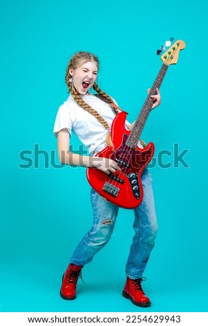 One Expressive Caucasian Teenager Guitar Player With Red Shiny Bass Guitar Posing In Casual White Shirt Showing Pleased Expression On Turquoise Background.Vertical Shot