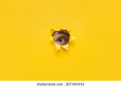 One eye looking through a hole in a yellow paper. Voyeurism. Woman is watching the husband. A curious look. Jealousy, spying on or overhearing the concept. Copy space. - Shutterstock ID 2077691914