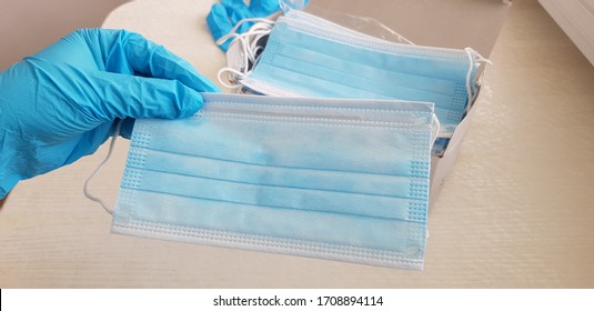 One Face Protection Mask In Human Hand Wearing Blue Surgical Glove Over Many Other Masks In A Box