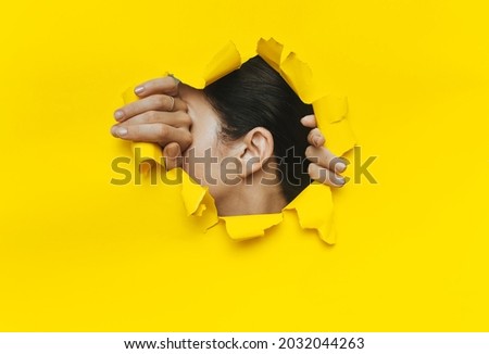 One female ear and two hands close-up. Copy space. Torn paper, yellow background. The concept of eavesdropping, espionage, gossip and the yellow press.