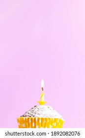 One festive cupcake in paper cup with yellow candles with flame for birthday on pink background copy space greeting card