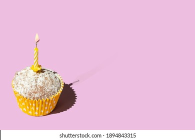 One festive cupcake in paper cup with yellow candle surprise birthday on pink background copy space greeting card