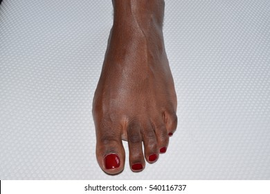 One foot of an African American woman with red toenails on white background