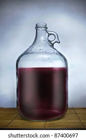 One Gallon Glass Jug Filled With Wine, Set On A Table With Blue Background